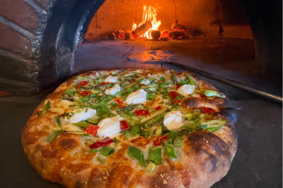 Fresh pizza in front of the wood-fire brick oven it was baked in.